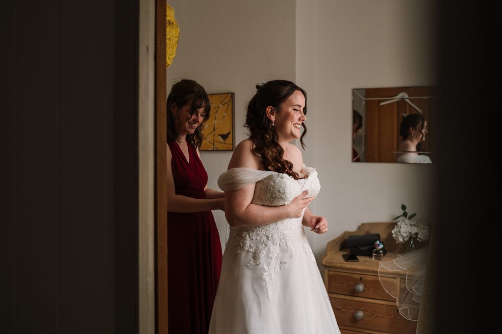 Photo of Bridesmaid helping Bride into dress in Taunton